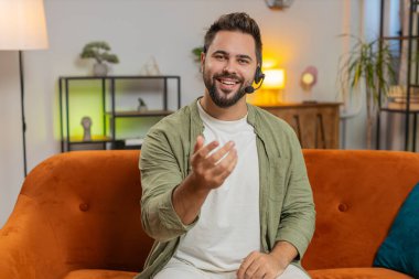 Kendine güveni tam, beyaz bir adam evdeki koltukta otururken kulaklık takıyor, serbest çalışıyor, çağrı merkezi, destek operatörü yardım hattı, müşteri ya da iş arkadaşıyla konuşuyor, iletişim desteği kullanıyor..