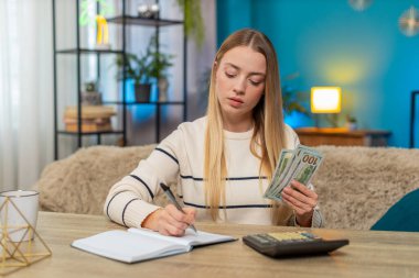 Masadaki beyaz kadın nakit sayıyor, hesap makinesi kullanıyor, not defterine yazıyor, maaştan çok emin. Kız mutlu görünüyor, tatmin olmuş, geliri, para yönetimi, planları var.