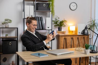 Mutlu genç iş adamı hevesle nişancılık oynuyor ya da akıllı telefondan video oyunu oynuyor masasında oturuyor ve ofisten çalışıyor. Tarz sahibi, serbest çalışan, e-öğrenen, internetten uzak bir iş..