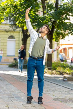 İletişim sinyalini yakalamaya çalışan genç bir turist, cep telefonundaki internet şehir sokaklarında daha iyi bir bağlantı için akıllı telefonu açtı. Hüsrana uğramış yetişkin erkek gezgin kasabada dikiliyor..