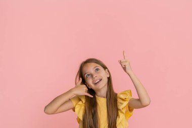 Genç kız bana işaret ederek, birini beni araması için çağırıyormuş gibi yaparak, reklam vermek için boş alana bakarak, neşeli bir gülümsemeyle işaret ediyor. Pembe arka planda izole edilmiş okul çocuğu.