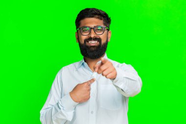 Hintli adam doğrudan kameraya bakar kendine güvenen bir gülümsemeyle, kişisel tercihini belirterek, sıranın sende olduğunu söyler. Yeşil renk arka planda izole edilmiş Arap adam karar ve seçim jestini gösteriyor