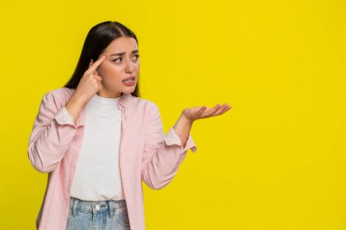 Genç bir kadın şakağına alaycı bir yüzle dokunuyor. İnanmadığını ve aptalca bir fikre karşı eleştiri yaptığını gösteriyor. Sarı arka plandaki kız saçmalıklara ve zeka yoksunluğuna tepki gösteriyor.