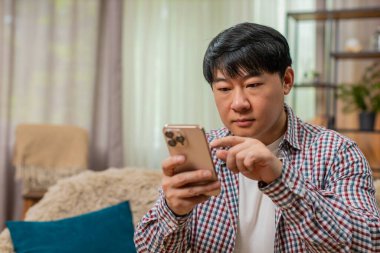 Kanepede oturan Asyalı adam akıllı telefondan internet formunu dolduruyor. Dikkatlice ekrana dokunuyor ve ciddi bakışlar atıyor. Çinli adam dijital uygulama sırasında hataları önlemek için özenli konsantrasyon gösteriyor.