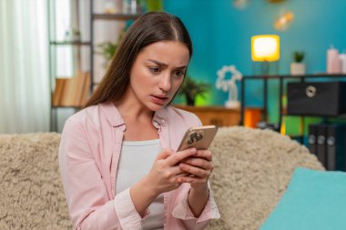 Genç bir kadın evdeki kanepede oturmuş akıllı telefon konuşmaları yapıyor ve olumsuz mesajlara sinirle el sallıyor. Kafkasyalı kız, internet üzerinden kelimelere tepki gösteren hoşnutsuz görünüm ve duruş gösteriyor..