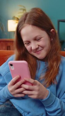 Neşeli genç kız, internet üzerinden akıllı telefon sosyal medya uygulamalarında rahatlama filmi izlerken mesajlarını paylaşıyor. Oturma odasında cep telefonu kullanan beyaz bir kız çocuk kanepede oturuyor..