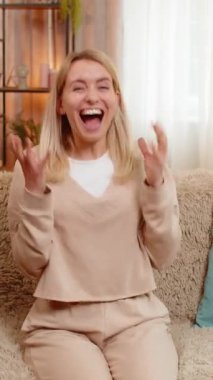 Kendine güvenen mutlu bir gülümsemesi olan genç bir kadın evinde koltukta otururken zaferi kutluyor. Sarışın kız neşe ve kişisel başarısını ifade eder, amaca ulaşmak ya da oyunu kazanmak için duygusal tepki verir..