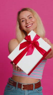 Mutlu gülümseyen genç bir kadın doğum günü hediyelerini sunar ellerini uzatır, hediye paketi sunar kariyer ikramiyesi teklif eder, kutlama partisi düzenler, indirim indirimi yapar. Sarışın kız pembe arka planda izole edilmiş.