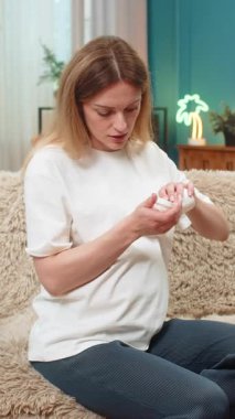 Hamile orta yaşlı kadın evde vitamin tableti yutuyor su içiyor sonra da rahatlama yardımı ile iç çekiyor. Kanepede gülümseyen beyaz kız günlük hapların anne ve bebeğin sağlığını desteklediğini biliyor..