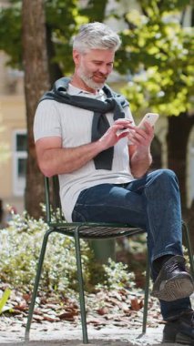 Akıllı telefonları kullanan, mesajlar yazan yakışıklı bir adam internetteki sosyal medya uygulamasını araştırmaktan ve dışarıda sohbet etmekten yoruldu. Şehir sokağındaki adam. Yaşam Tarzları.