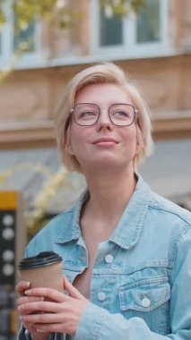 Kafkasyalı genç, mutlu sarışın kadın sabah kahvesinin tadını çıkarıyor sıcak bir şeyler içiyor ve dışarıda gülümsüyor. Dinleniyorum, ara veriyorum. Şehir merkezi caddesinde yürüyen ve kahve içen bir kız. Kasaba yaşam tarzları.