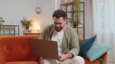 Tartışma. Öfkeli, sinirli, serbest çalışan genç adam koltukta oturmuş hararetli sohbetlere dalıyor. Kafkasyalı erkek, apartman odasındaki kanepede dizüstü bilgisayar kullanarak hayal kırıklığı yaşıyor..