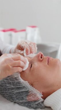 Kozmetik doktoru, temizlikçi kadın yüzü, kaplıca salonundaki pamuklu mendilli gözler. Kız teninin kozmetik güzellik prosedüründen önce temizlenmesi. Güzellik uzmanından yüz bakımı. Dikey yakın plan portre