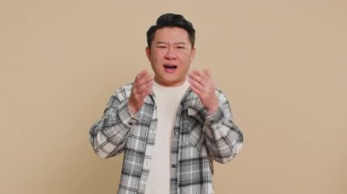 Duymak istemiyorum, dinle. Sinirli, sinirli Asyalı adam kulaklarını kapatıyor hayır diyor, tavsiyelerden kaçıyor gürültülü sesleri duymazdan geliyor. Çinli olgun adam bej arka planda izole edilmiş.