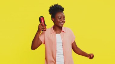 Afro-Amerikalı kadın kırmızı portatif hoparlör tutuyor, müziğin ritmine enerji katarak kolayca hareket ediyor. Sarı arka planda izole edilmiş siyah bir kız favori melodilerin keyfini çıkarırken keyif rahatlığı gösteriyor.