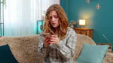 Evde bekleyen genç bir kadın, uzun zamandır akıllı telefondan neşe ve heyecanla gülümseyen bir mesaj alıyor. Kanepede oturan beyaz saçlı kız mutlu, neşeli ve duygusal tepki veriyor..