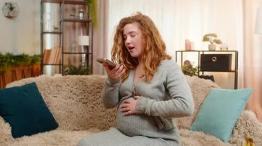 Hamile genç bir kadın akıllı telefonuyla sesli mesaj kaydediyor, gülüyor ve el kol hareketi yapıyor, olumlu duyguları ve bağlantıları paylaşıyor. Kız her anın tadını çıkarıyor, mutluluğu ve beklentiyi kucaklıyor.