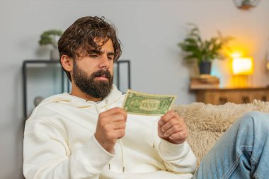 Zavallı Hintli Arap 'ın portresi bir dolar banknotunu gösteren yetersiz miktarda para yüzünden üzgün. Finansal kriz. İflas. Yoksulluk. Evdeki kanepede oturan üzgün İspanyol adam..