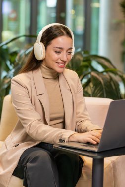 Happy, modern ofis lobisinde dizüstü bilgisayarda çalışırken, kablosuz kulaklıklı, dans eden, rahatlatıcı müzik dinleyen, neşeli, Kafkasyalı genç iş kadını. Otel odasında oturan bayan.