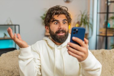 Akıllı telefon kullanan genç Hintli sakallı bir adam, iyi haber mesajı alıyor, piyango zaferini kutlarken şok oluyor evdeki kanepede oturma odasında büyük ikramiyeyi kazanıyor. Yaşam Tarzları.