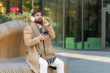 Kablosuz kulaklıkla dans eden mutlu, rahat Hintli genç işadamının portresi, akıllı telefon dansında enerjik disko müziği dinlemek. Şehir merkezindeki bankta oturan İspanyol sakallı adam.