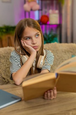 Evde kanepede oturan genç kız, ne yazık ki ödevi anlamak için mücadele eden okul kitabına bakıyor. Okul çocuğu, ev ödevi sırasında hayal kırıklığı ve zorluk göstererek kafasını karıştırıyor.