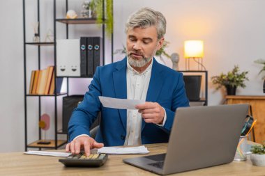 Merkez ofisteki orta yaşlı işadamı bugün hesap makinesi tarama makbuzlarını kullanarak bütçeyi gözden geçiriyor. Masa girişindeki serbest çalışan adam, para akışı bakiyesi tahmini giderlerini ayarlıyor.