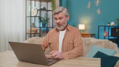 Laptop kullanan mutlu beyaz adam önemli bir e-posta mesajına ulaşıyor. İyi haber. Tatmin olmuş orta yaşlı bir adam evinde oturmuş sevinçle bağırıyor, oyunu kazandıktan sonra ellerini kaldırıyor.