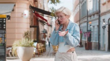 Kızgın kızgın kızgın, Avrupalı genç bir kadın telefonda tartışırken sinirli bir şekilde dışarıda bağırıyor. Şehir caddesinde sarı saçlı, hoşnutsuz, kızgın bir kızı gücendirdim. Kasaba yaşam tarzları.