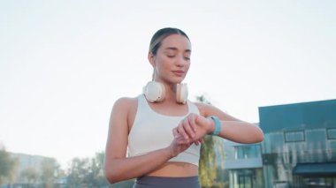 Atletik koşucu yetişkin kız akıllı saat düzeneği bileziğine bakar zamanı, kalp atışını, nabzı, koşudan sonra SPO2 'yi kontrol eder. Sabah şehir parkında kardiyo yapan bir kadın..