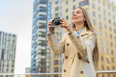 Hafta sonları şehir keşfi yapan orta yaşlı mutlu kadın turist dışarıda antika kameralarda fotoğraf çekiyor. Şehir sokağında tatilde uzun paltolu bir kız. Yaşam Tarzları.