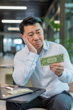 Depresyondaki Çinli işadamı maddi sorunlar hakkında endişeli. Tişörtlü stresli adam hayal kırıklığına uğramış görünüyor. Para borcu, kötü bir gün, bütçe kaybı, iflas modern ofis lobisinde oturuyor..