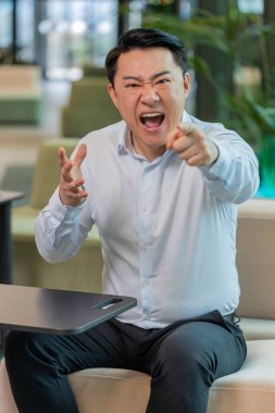 Tişörtlü kızgın yetişkin patron ofisteki modern işyerindeki kameraya bakarak video konuşması yapıyor. Tatminsiz Çinli iş adamı, şirket sorunları hakkında astlarıyla iletişim kuruyor..