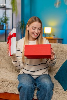 Modern evde koltukta oturan mutlu beyaz kadın doğum günü sürprizi kutusunu açıyor mutlu mutlu mutlu bir jest. İçerideki neşeli anın tadını çıkarıyorum. Duygusal sıcak hava enerji kutlaması.
