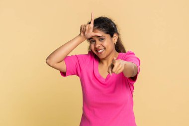 Hintli kadın komik bir şekilde L eziğinin alnına imza attırıyor, ironik bir şekilde gülümsüyor, dalga geçiyor. Bej arkaplanlı bir kız ironiyi, mizahı, alaycılığı, şakayı, alay etmeyi ya da şakayı ya da şakacı bir hareketi gösterir..