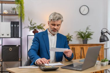 Merkez ofisteki orta yaşlı işadamı bugün hesap makinesi tarama makbuzlarını kullanarak bütçeyi gözden geçiriyor. Masa girişindeki serbest çalışan adam, para akışı bakiyesi tahmini giderlerini ayarlıyor.