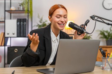 Merkez ofisteki genç iş kadını stüdyo mikrofonuna podcast blogunda gülerek konuşuyor. Dizüstü bilgisayarın yanındaki serbest çalışan kız fikirleri paylaşıyor ve eğlenceli işlerin tadını çıkarıyor..