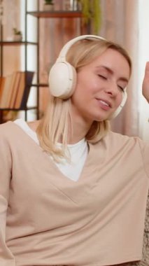 Genç yetişkin bir kadın evdeki kanepede kablosuz kulaklıklarla oturuyor ve huzurlu bir ifadeyle yavaşça müziğe doğru sallanıyor. Mutlu kız ritm sakinliğinden hoşlanıyor, tamamen rahatlamış ve dengeli duygusal ruh haline dalmış.