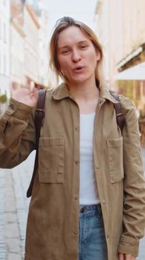 Kameraya gülümseyen kız turistin portresi, el sallayarak davetiye, selam, selam, güle güle, misafirperver bir yüz ifadesiyle karşılama. Şehir merkezindeki kadın..