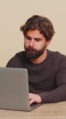 Genç aşırı çalışan adam dizüstü bilgisayardaki sıkı çalışmadan sonra bitkinlik ve yorgunluk hissediyor. Adam bilgisayarı kapatıyor ve kafasını masaya yaslayarak rahatlamaya çalışıyor. Bej renkli stüdyo geçmişi olan adam..