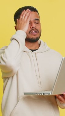 Memnun olmayan Hintli adam dizüstü bilgisayar kullanıyor. Bilgisayarda arama yapıyor. Piyango kötü sonuçlara şaşırıyor. Sarı arka planda izole edilmiş Arap adam.