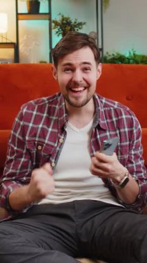 Heyecanlı genç adam elinde akıllı telefon ile online bahis piyangosunun piyango ikramiyesi kazanmasıyla şaşırmış iyi haberler okuyor. Zaferden çok memnun olan mutlu Kafkasyalı adam evde başparmak kaldırıyor.