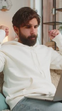 Dizüstü bilgisayar kullanan heyecanlı Hintli genç adam, posta yoluyla iyi haber mesajı alıyor, evdeki kanepede piyango kazanma ikramiyesini kutlarken şaşkınlığa uğruyor. Yaşam Tarzları.