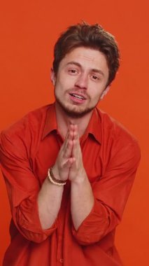 Lütfen, Tanrım yardım et. Beyaz adam kameraya bakarak ve dilek tutarak dua ediyor, umut dolu bir ifadeyle soruyor, özür diliyor, meditasyon yapıyor. Yakışıklı adam turuncu stüdyo geçmişinde izole edilmiş.