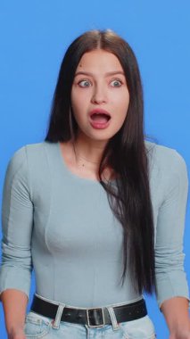 Aman Tanrım, vay canına. Heyecanlı kazanan kadın şaşkınlıkla el kaldırıyor. Büyük gözleriyle kameraya bakıyor. Ani zaferden şok oluyor. Mavi stüdyo arka planında yalnız, samimi, çekici bir kız.