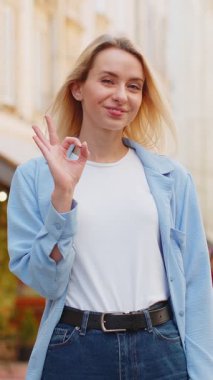 - Tamam. Mutlu, genç, beyaz bir kadın kameraya olumlu bakıyor işaret gibi olumlu bir hareket sergiliyor, güzel bir kutlama zaferini onaylıyor. Şehir caddesinde duran neşeli bayan.