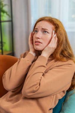 Hasta kızıl saçlı kadın baş ağrısı problemini tedavi etmek için tapınakları ovuyor, tansiyon ve migren stresinden muzdarip evde acı içinde kıvranıyor yüksek tansiyon. İçerideki küçük kız kanepede yatıyor. Dikey