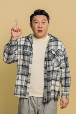 - İyi fikir. Asyalı ilham verici bir adam, ağzı açık bir şekilde işaret ediyor, plan yapıyor, işe koyuluyor, Eureka jest problemi çözümü için ilham veriyor. Çinli adam bej renkli stüdyo arka planında izole edilmiş.