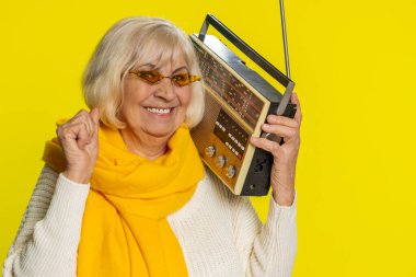 Yaşlı bir kadın müzik dinlemek için retro kaset çalar kullanıyor, disko dansı favori şarkıları, eğleniyor, eğleniyor, klasik teknolojilerin hayranı. Sarı arka planda olgun bir büyükanne.