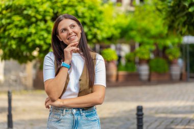Düşünceli gülümseyen mutlu esmer kadın, dalgın bir ifadeyle, bir çözüm düşünüyor, şüpheli bir soru soruyor, dışarıda hayaller kuruyor. Şehir caddesinde duran yetişkin kız..